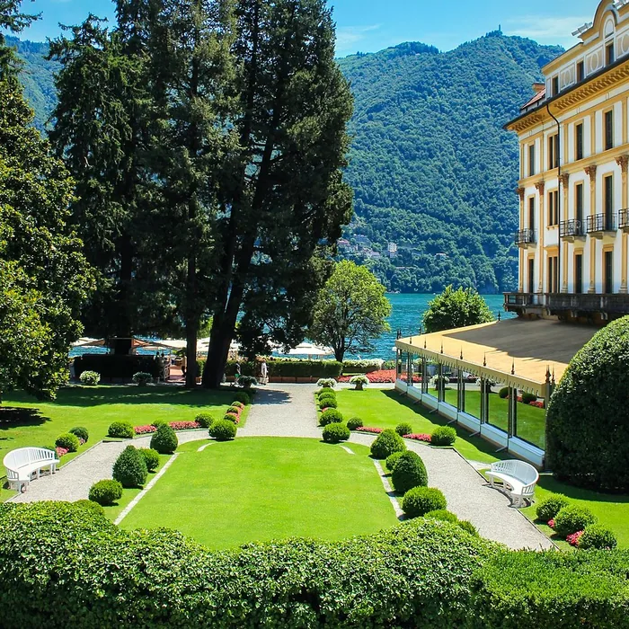 Giardino con prato, siepi basse e grandi alberi davanti a una villa